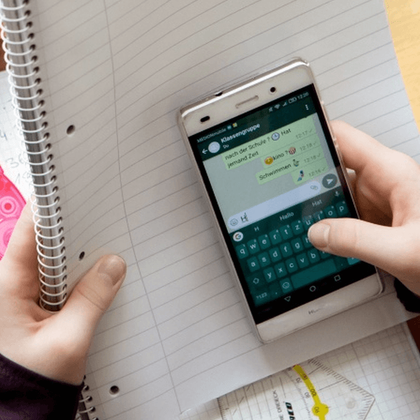 ein Kind hält ein Smartphone und ein Heft